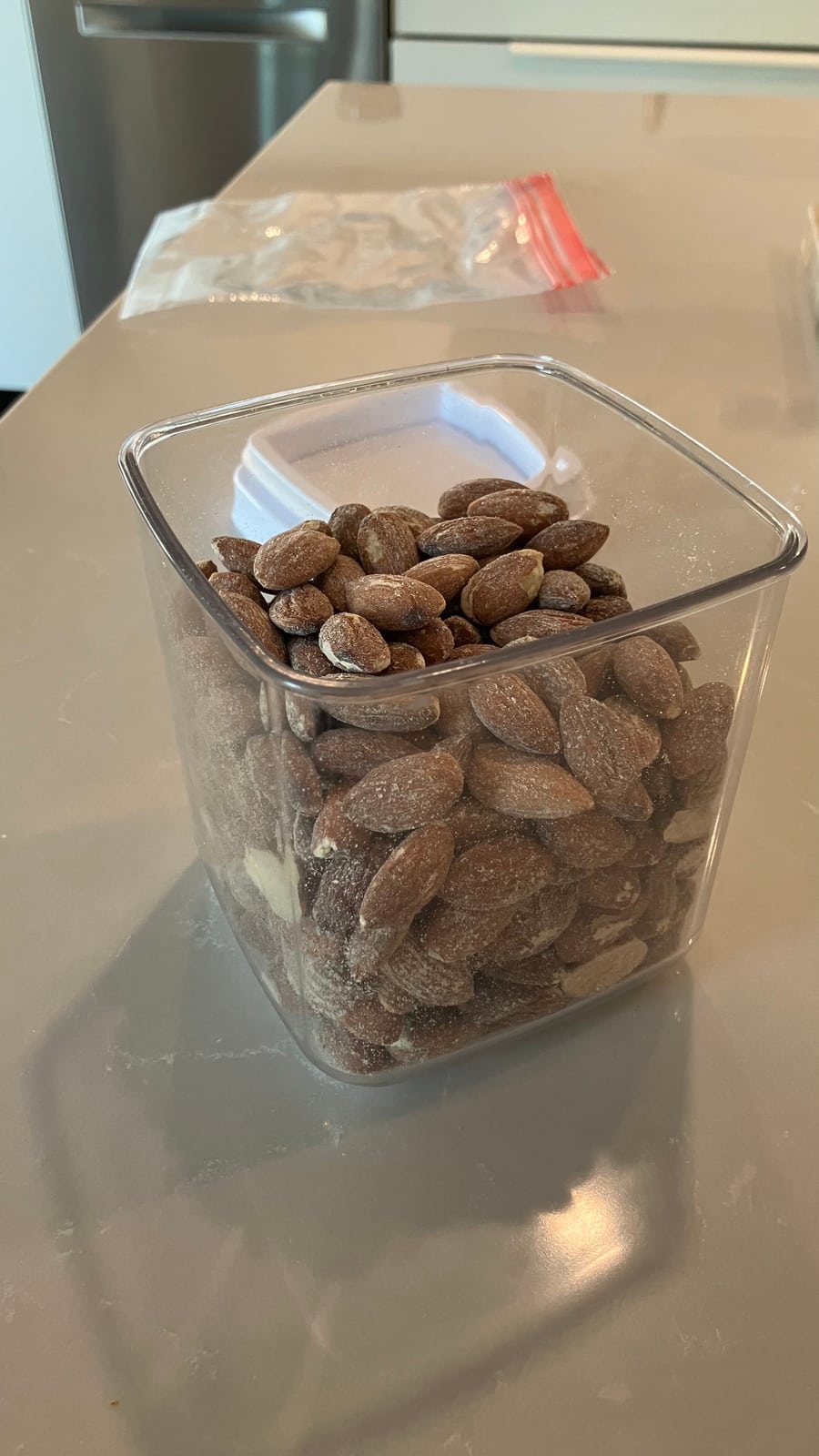 The same container with the lid off, showing almonds piled near the top and a plastic bag behind it