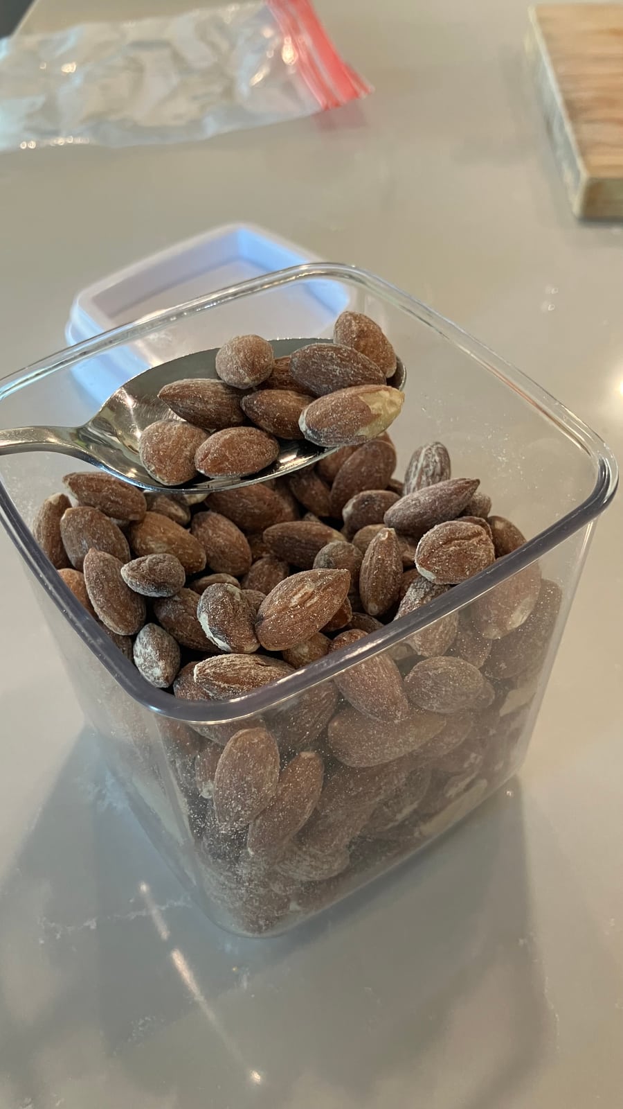 A spoon lifting almonds from the top of the pile in the clear container